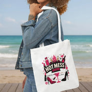Person holding a tote bag with 'Hot Mess' design on a beach