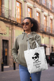 Woman holding a tote bag with a design and text on a city street.