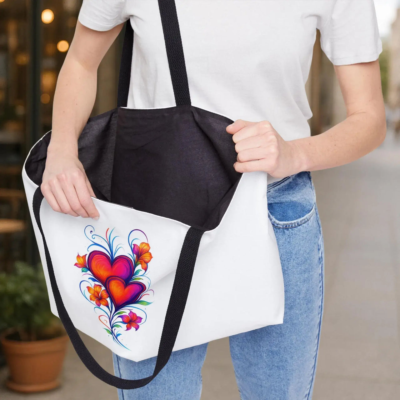 Person holding a tote bag with a colorful heart design outdoors