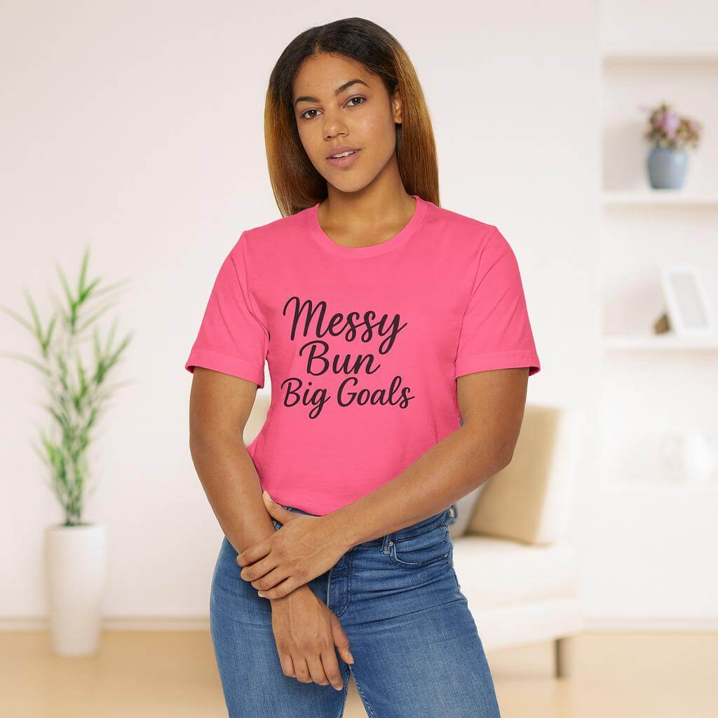 Woman wearing a pink t-shirt with 'Messy Bun Big Goals' text in a living room setting.