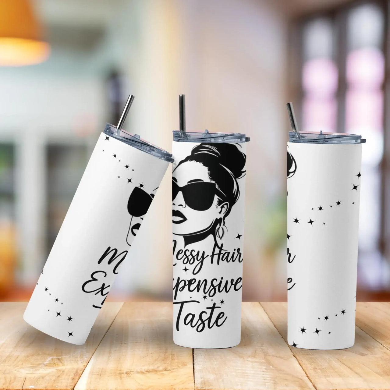 Three white tumblers with black text and a design of a woman with messy hair on a wooden surface.