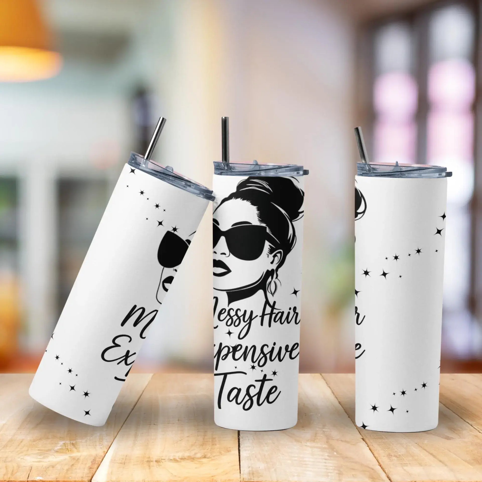 Three white tumblers with black text and a design of a woman with messy hair on a wooden surface.