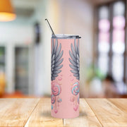 Tumbler with wing design on a pink background on a wooden table.