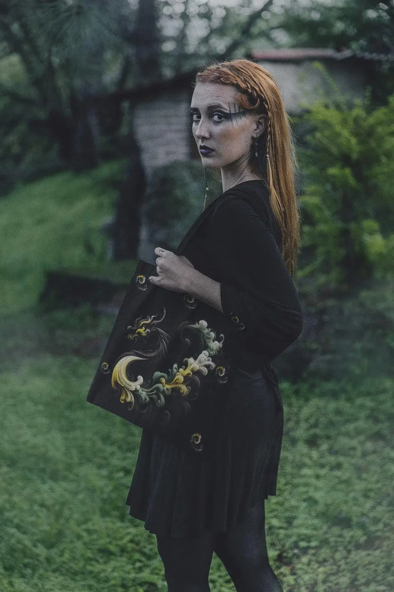 Person holding a black bag with decorative elements in an outdoor setting