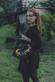 Person holding a black bag with decorative elements in an outdoor setting