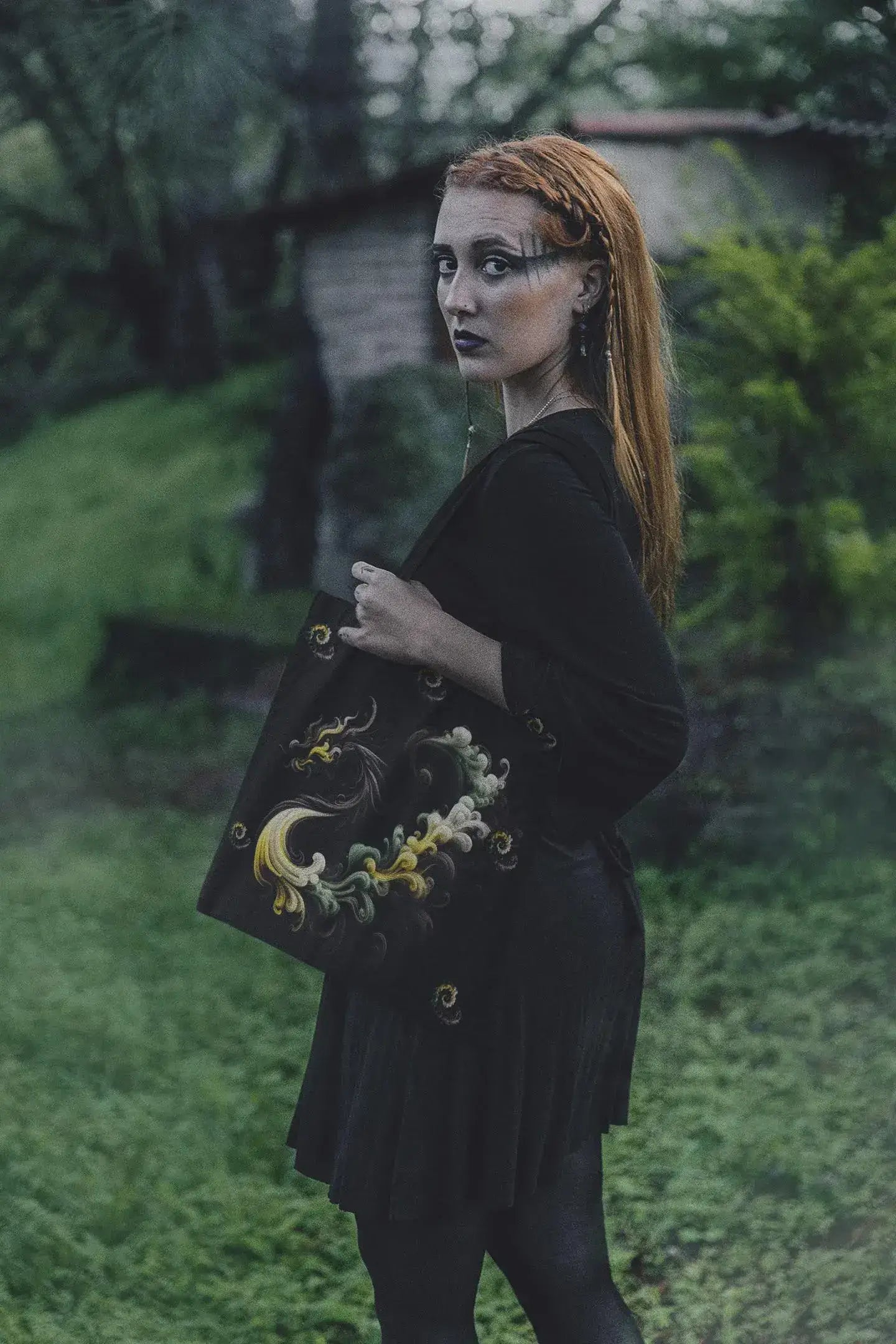 Person holding a black bag with decorative elements in an outdoor setting