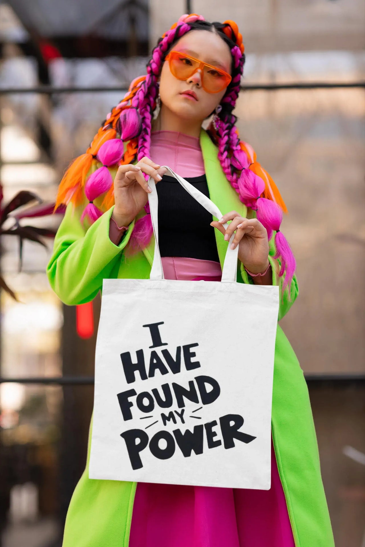 Person with colorful hair holding a tote bag with text, blurred background