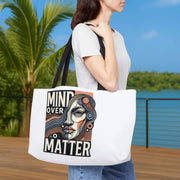 Person holding a tote bag with 'Mind Over Matter' design outdoors.