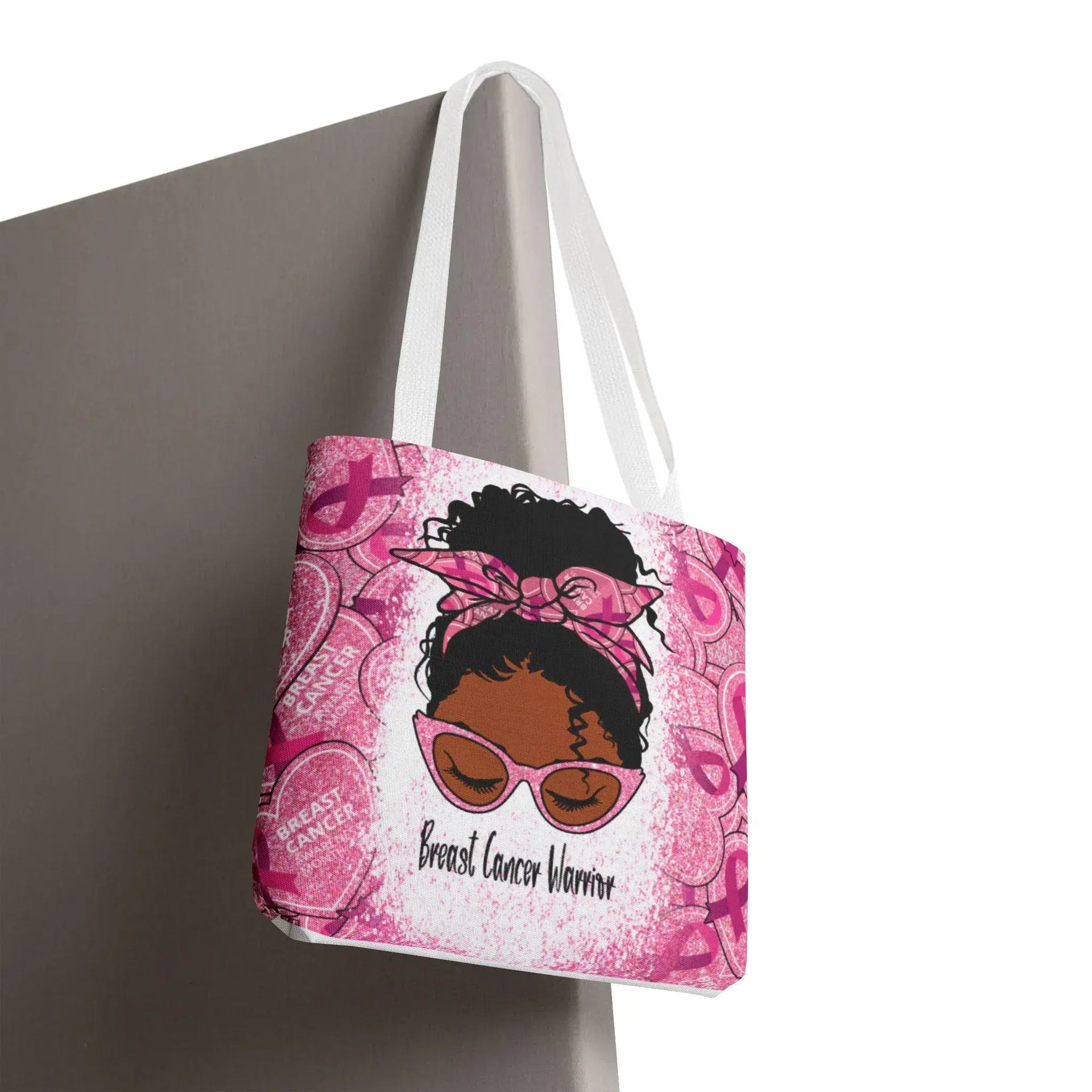 Pink tote bag with a graphic of a woman and 'Breast Cancer Warrior' text, hanging on a surface.