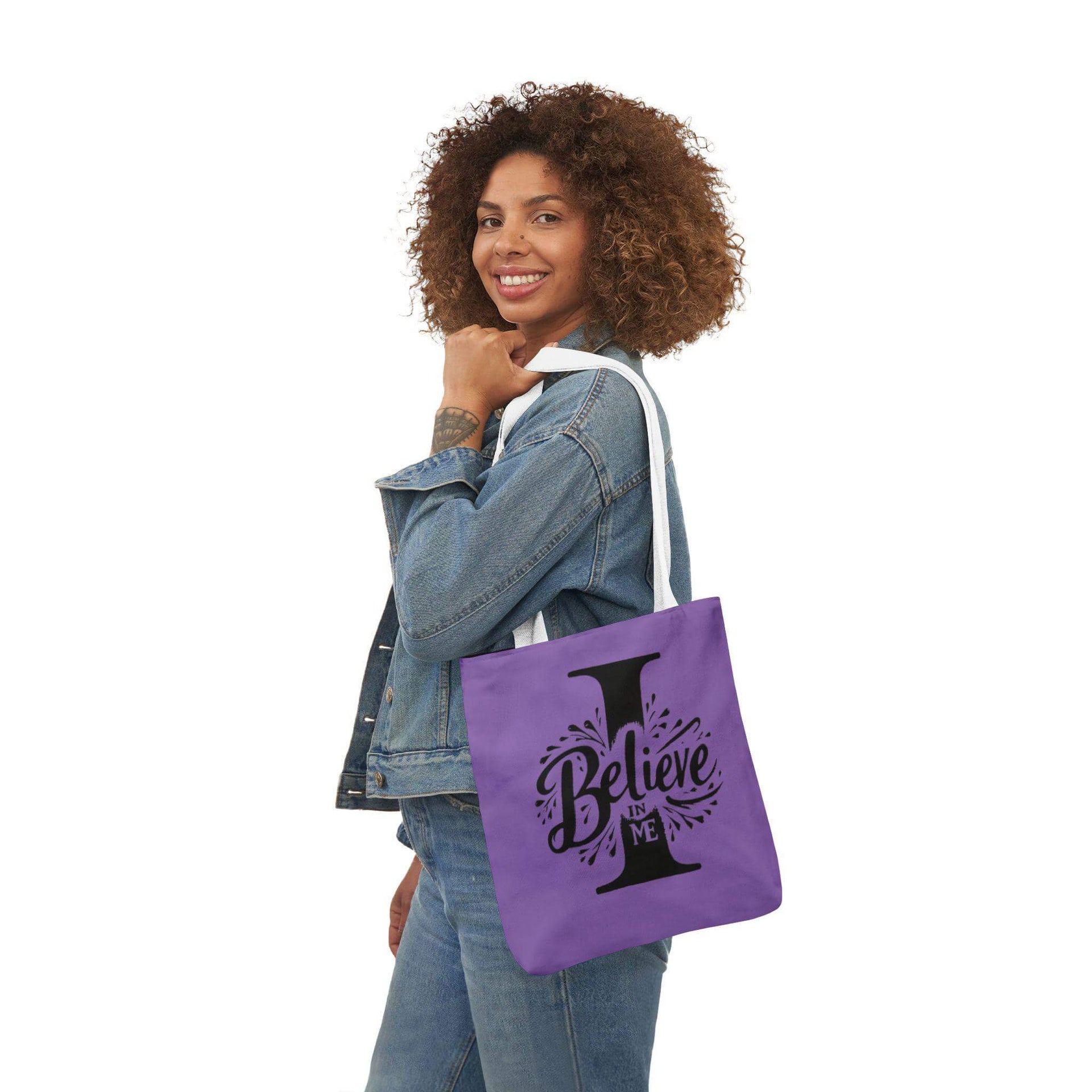 Woman holding a purple tote bag with 'I Believe' design on a white background