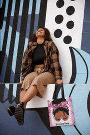 Woman sitting on a wall with a colorful abstract design, holding a tote bag with an illustration of a woman with a pink bow.
