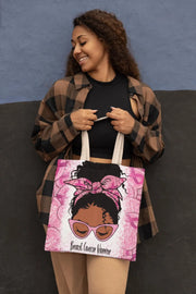 Woman holding a tote bag with a design of a woman with a pink headscarf and sunglasses, text 'Breast Cancer Warrior' on a blue and black background.