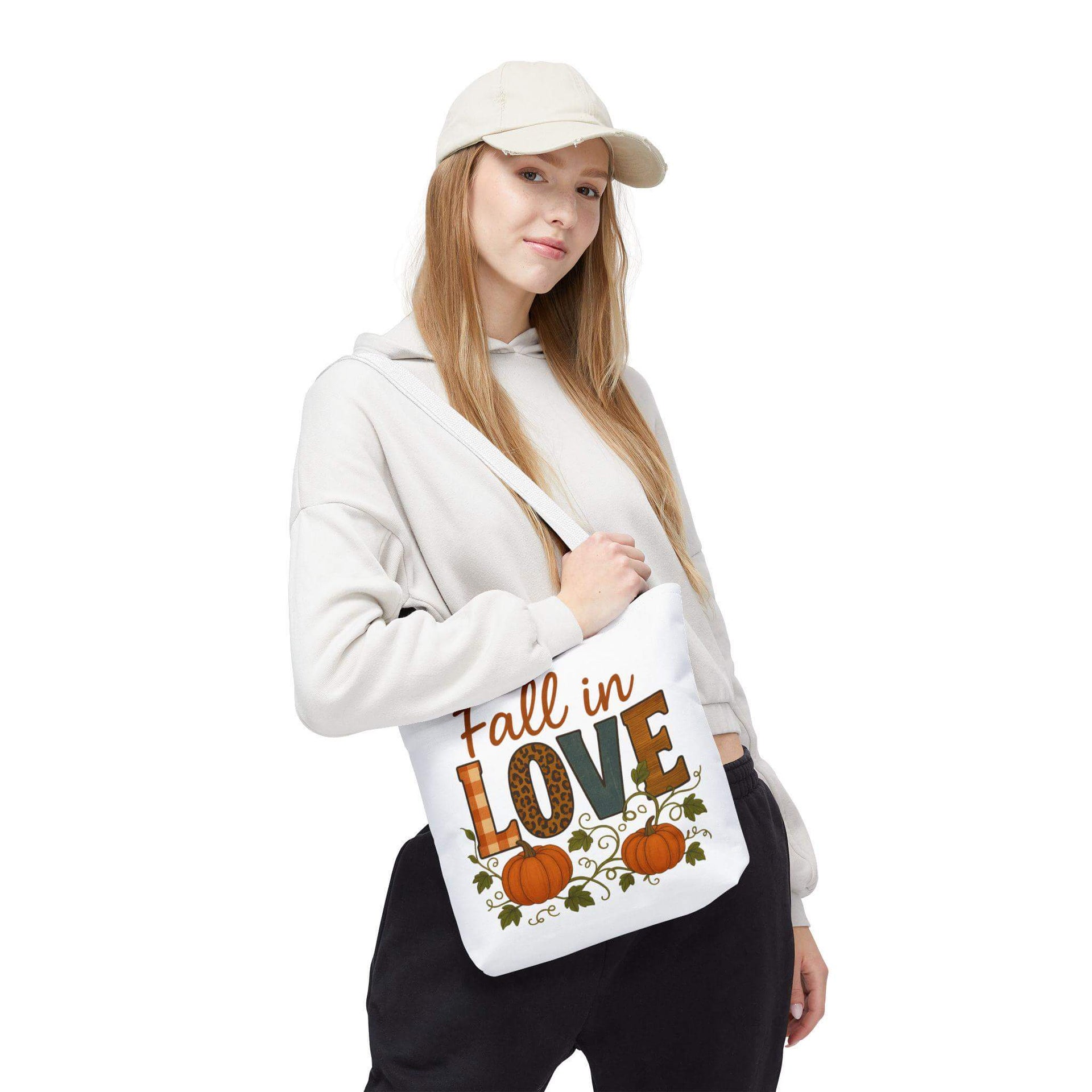 Person holding a tote bag with 'Fall in Love' text and pumpkins on a white background