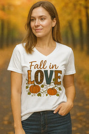 Woman wearing a white t-shirt with 'Fall in Love' and pumpkin design, standing in an autumn setting.
