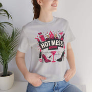 Person wearing a white t-shirt with 'Hot Mess' graphic design, standing indoors next to a plant.