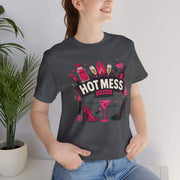 Person wearing a dark gray t-shirt with 'Hot Mess' graphic design, standing indoors next to a plant.