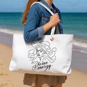 Person holding a tote bag with 'Divine Energy' design on a beach