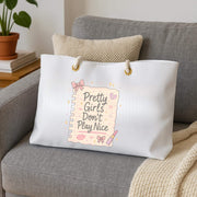 White tote bag with 'Pretty Girls Don't Play Nice' text on a gray couch.