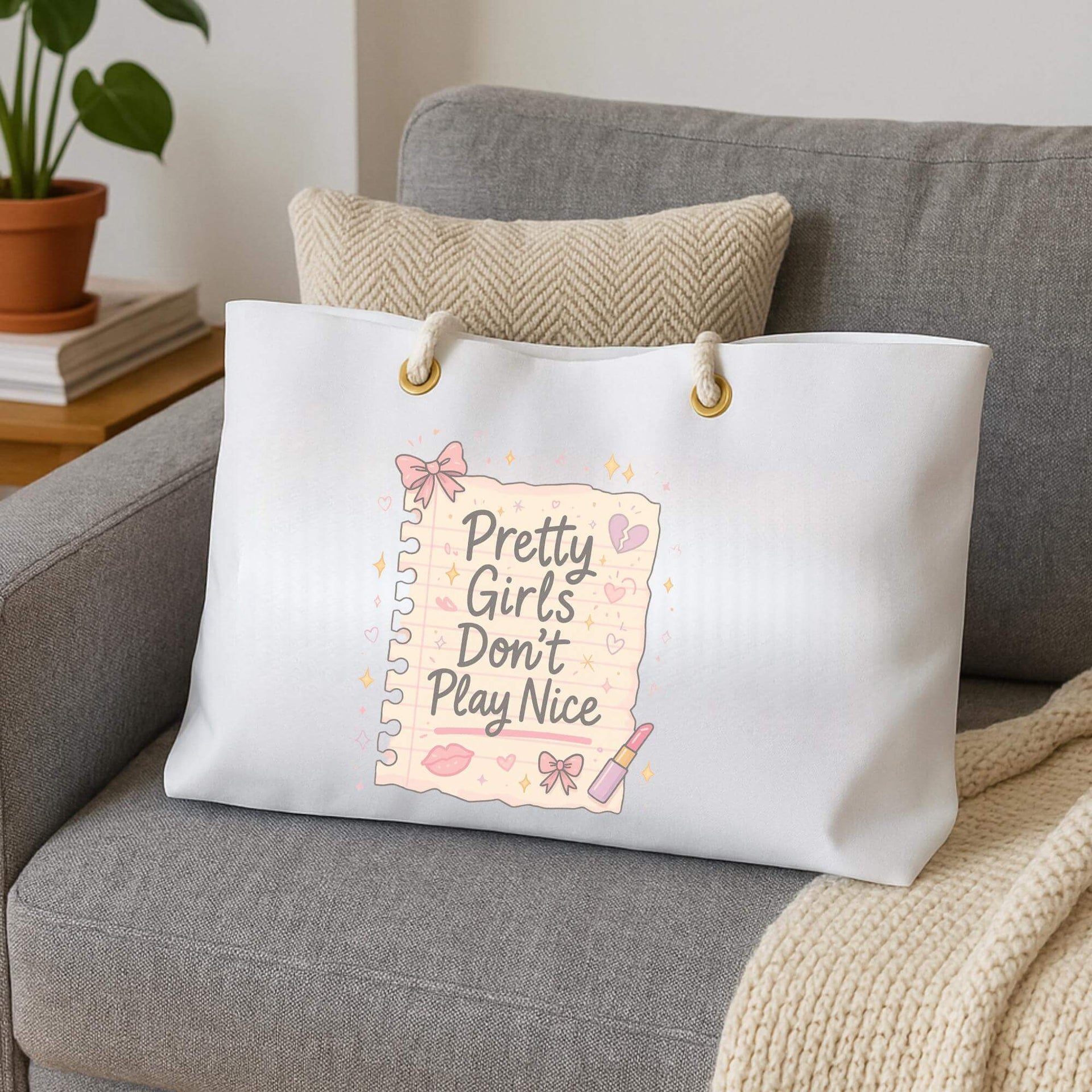 White tote bag with 'Pretty Girls Don't Play Nice' text on a gray couch.
