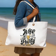 Person holding a tote bag with 'Wife of the Party' text on a beach