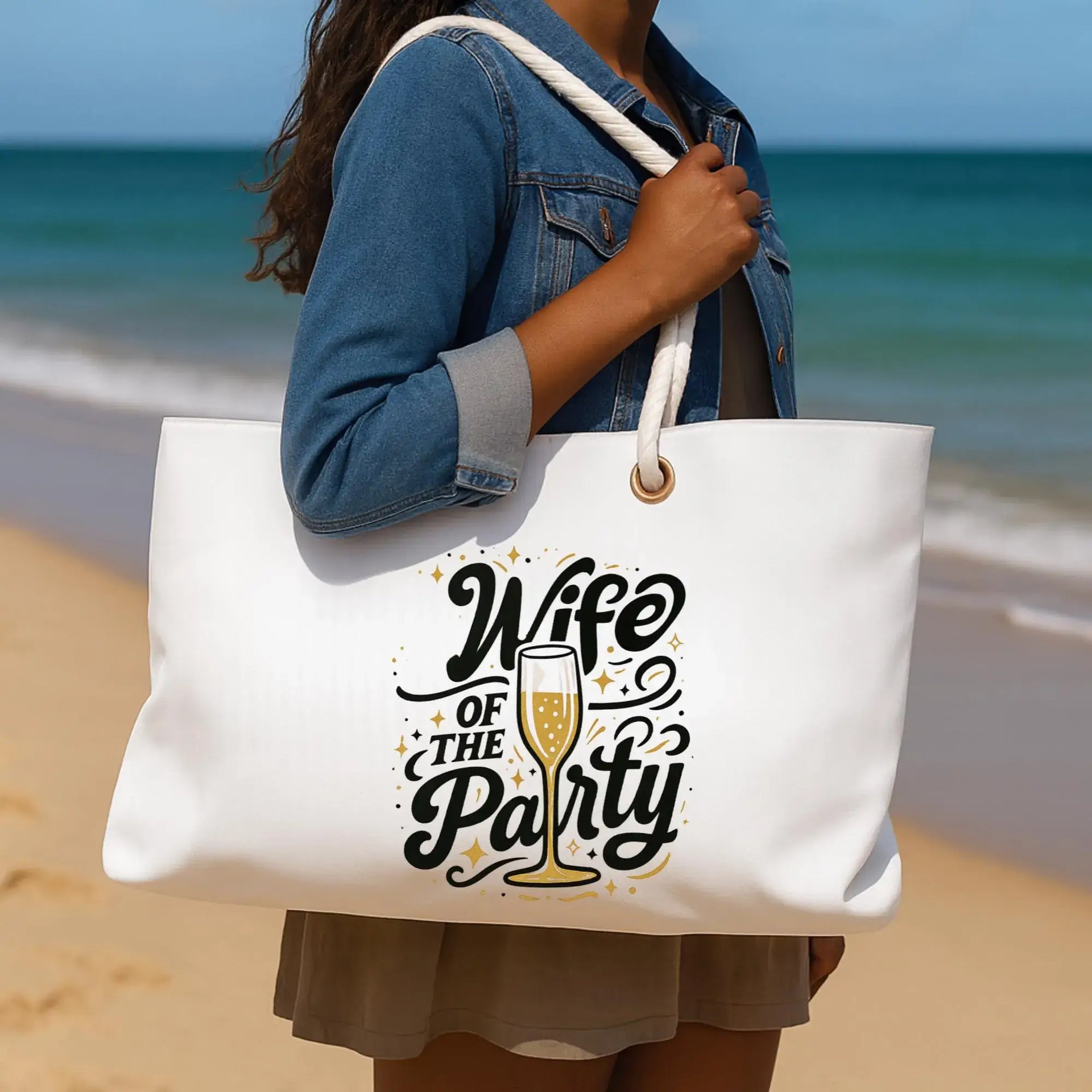 Person holding a tote bag with 'Wife of the Party' text on a beach