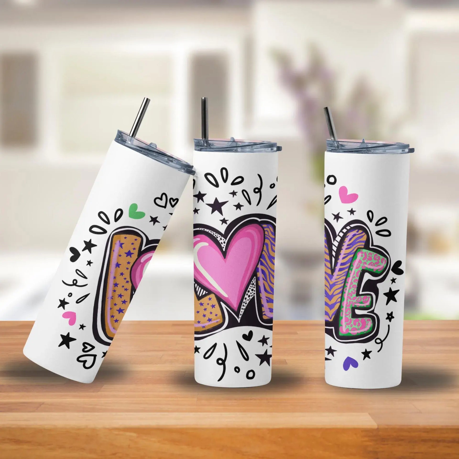Three insulated tumblers with colorful designs on a wooden surface.