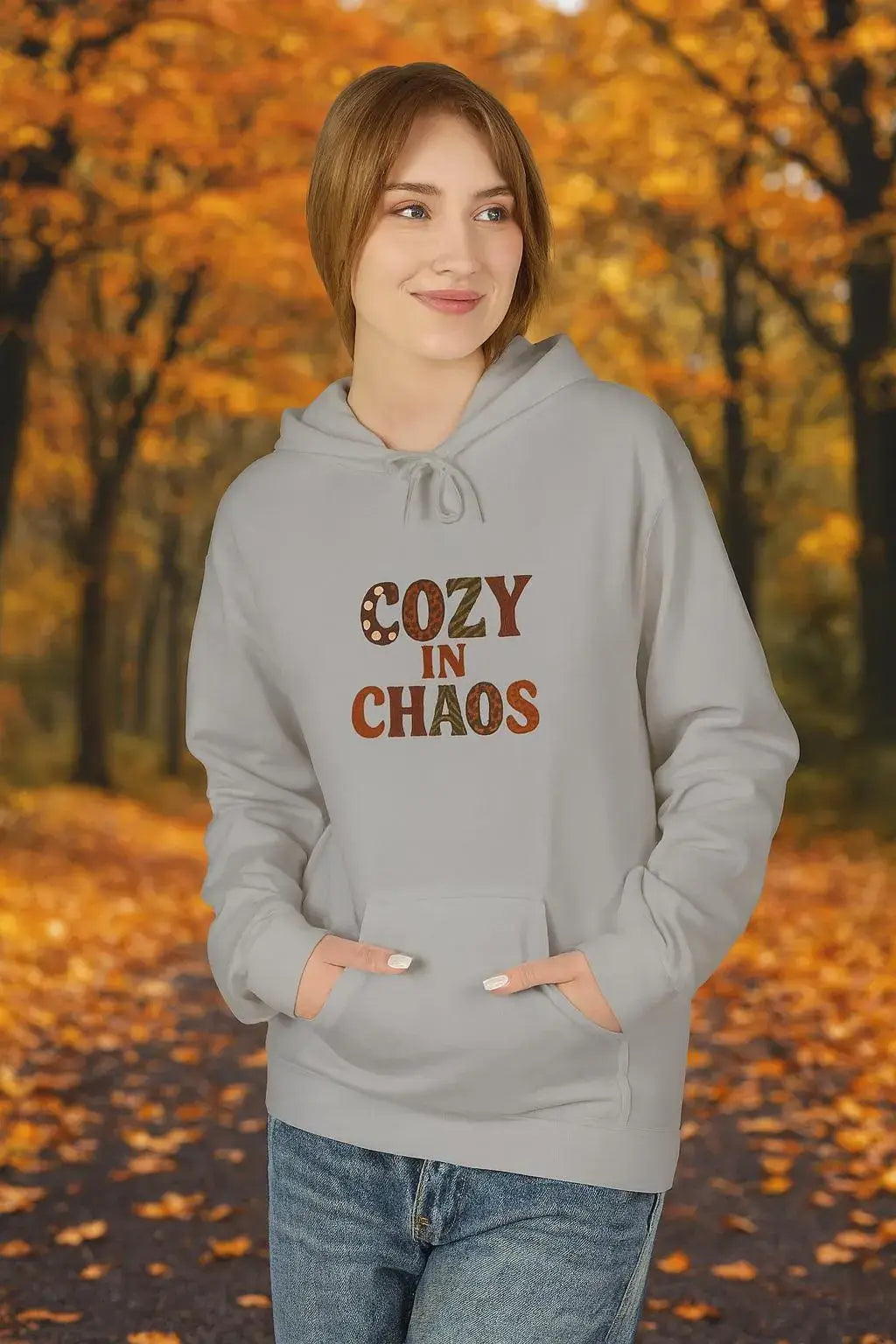 Person wearing a gray hoodie with 'Cozy in Chaos' text in an autumn setting