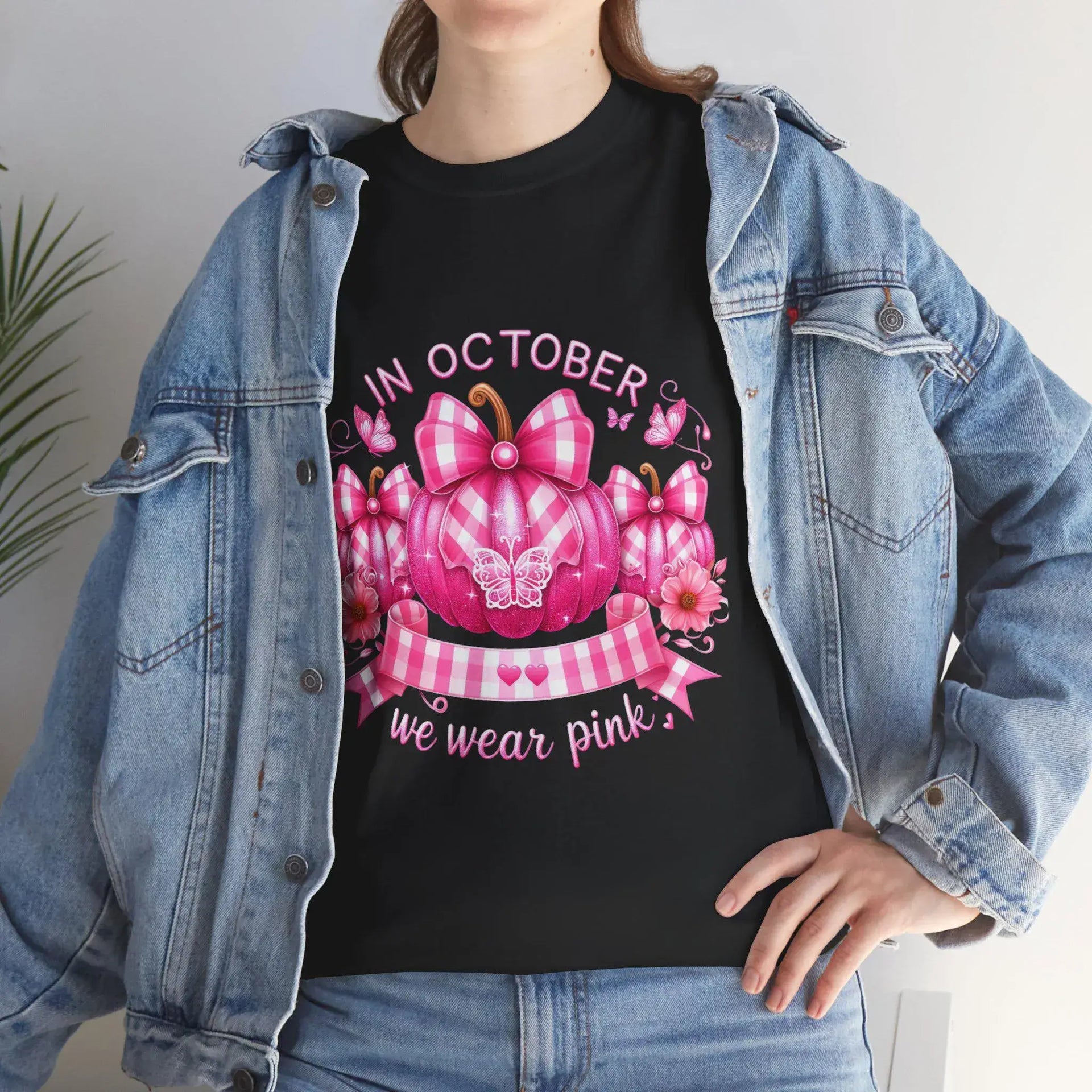 Person wearing a black t-shirt with a pink pumpkin design and 'In October we wear pink' text, paired with a denim jacket.